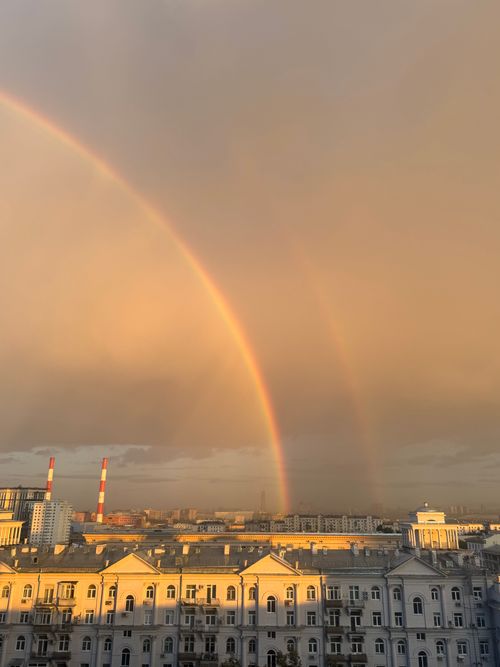 Free Vibrant double rainbow arches over urban skyline during sunset, casting golden light. Stock Photo