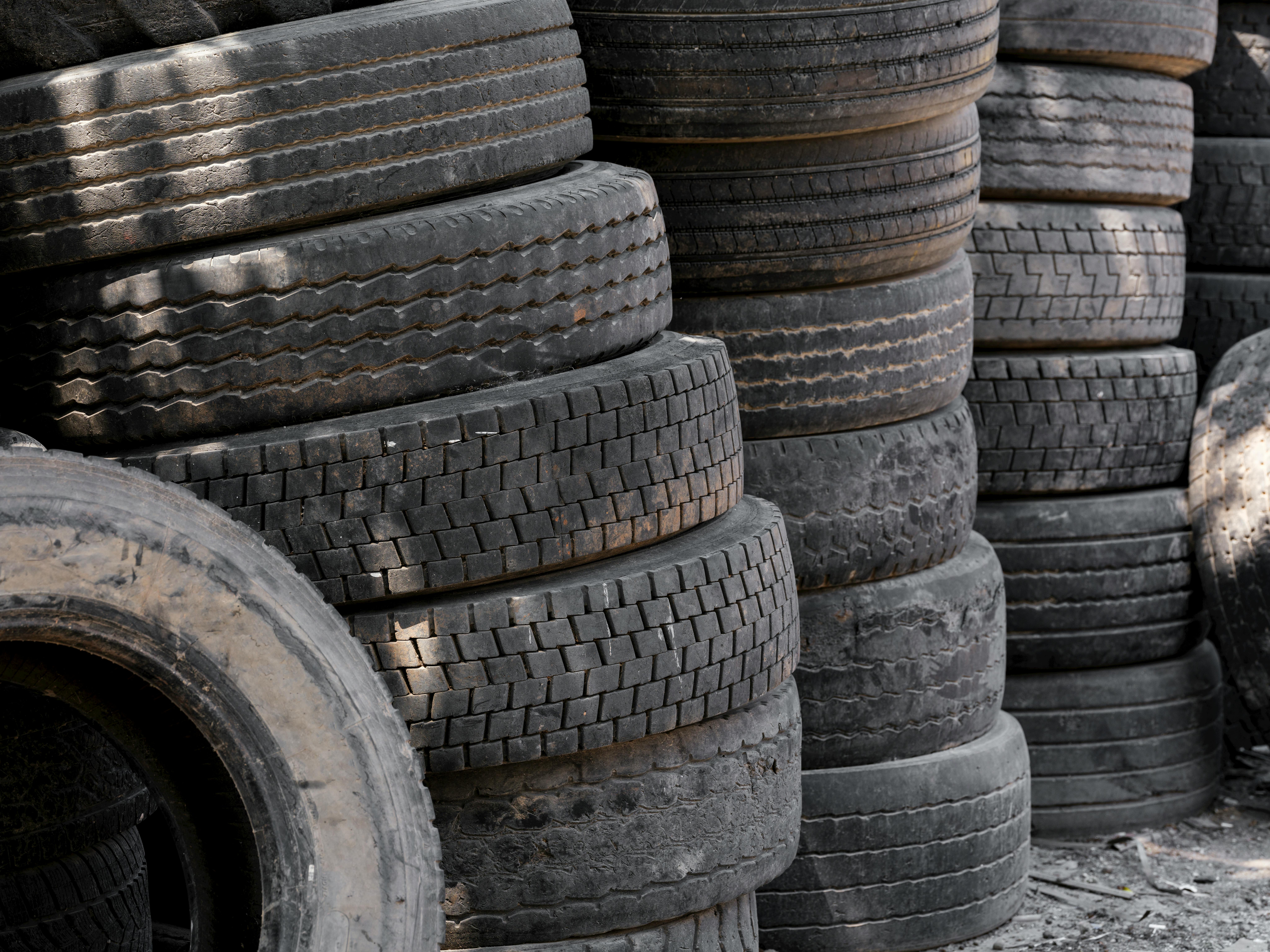 Piles of old tires stacked outdoors for recycling in an industrial environment.