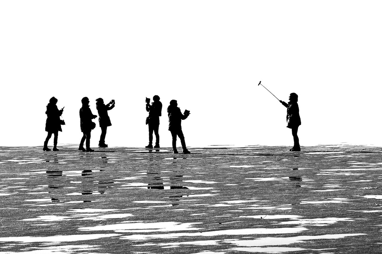 black and white silhouette of people on a reflective surface taking ph