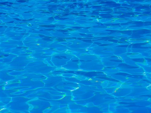 Free Relaxing view of a crystal clear swimming pool or resort water surface, reflecting sunlight. Stock Photo