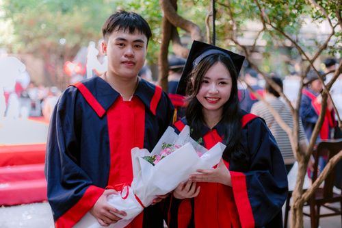 Free Two graduates in cap and gown celebrating outdoors, holding a bouquet. Stock Photo
