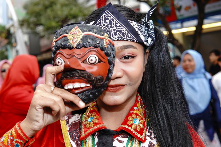 A woman in traditional attire holding a mask during a cultural festival in Bandung, Indonesia.