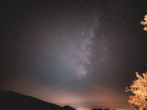 Free Captivating view of the Milky Way galaxy stretching across the night sky above silhouetted mountains. Stock Photo