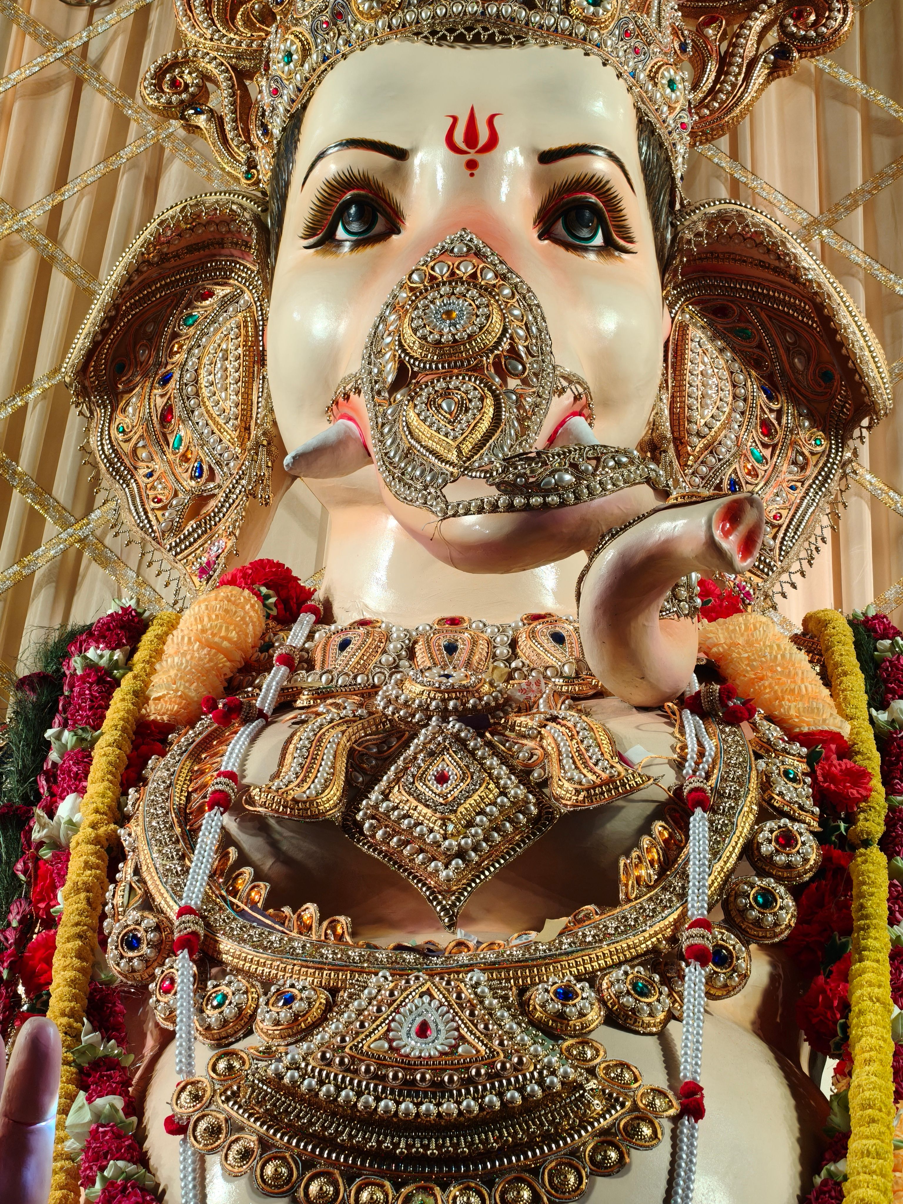 Close-up of an ornate Ganesha idol adorned with colorful decorations and jewelry in a festive setting.