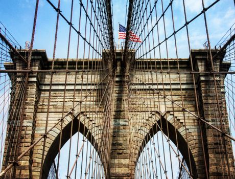 Dramatic view of the Brooklyn Bridge tower with cables and American flag.