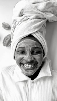 African woman enjoying spa day with facial mask and towel wrap, smiling warmly.