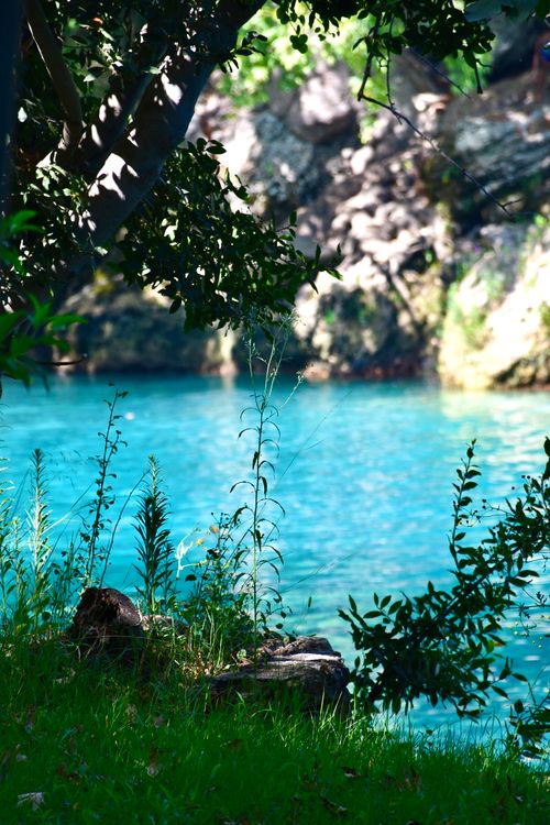 Free Peaceful riverside scene with lush greenery and bright blue waters, perfect for relaxation concepts. Stock Photo