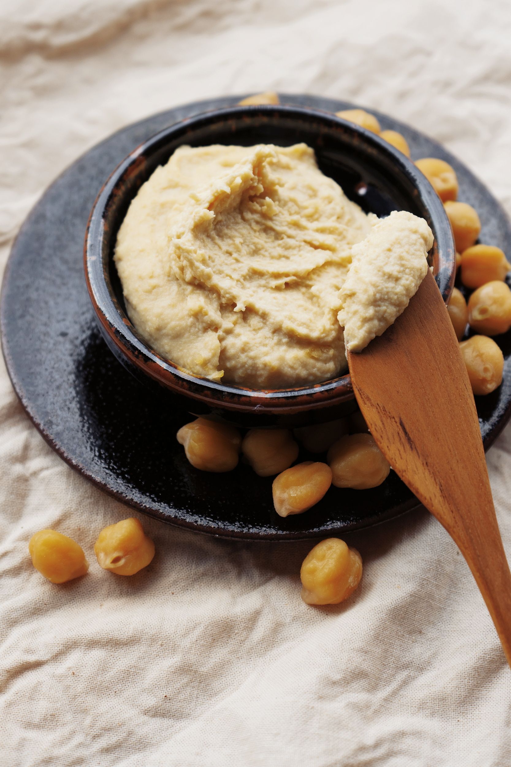 Delicious homemade hummus in a bowl with scattered chickpeas on a rustic background.