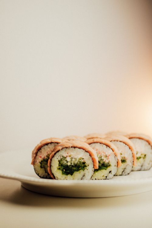 Free Close-up of fresh sushi rolls with avocado and salmon on a white plate, captured indoors. Stock Photo