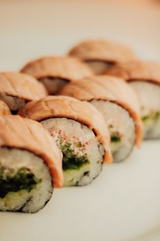 Close-up of delicious sushi rolls with salmon topping on a white plate.