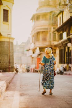 A senior woman in traditional attire walks through the historic streets of Indore, India, at sunrise.