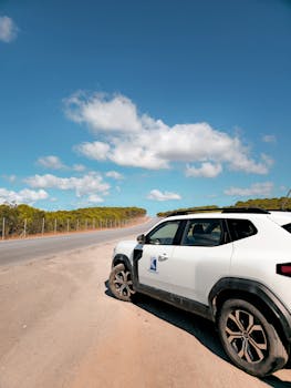 White SUV parked on a deserted road under a vibrant blue sky with fluffy clouds.
