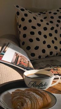 A relaxing morning setup with coffee, croissant, and a magazine on a couch.