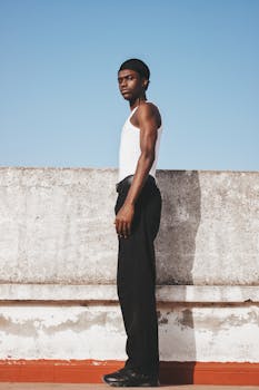 Side profile portrait of a man in casual attire standing against a clear blue sky. Urban fashion.