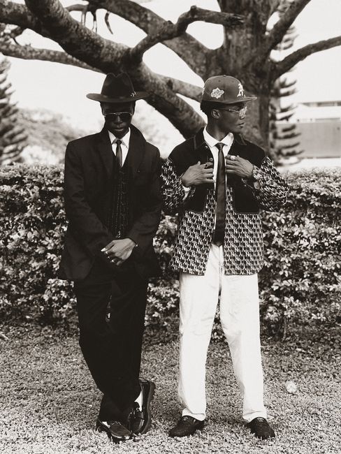 Two stylish men in vintage suits posing outdoors, exuding classic elegance.