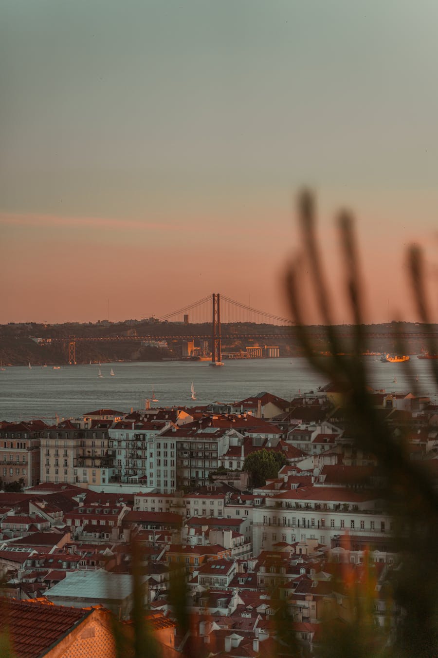 A stunning sunset view over Lisbon, featuring the iconic 25 de Abril Bridge and the cityscape
