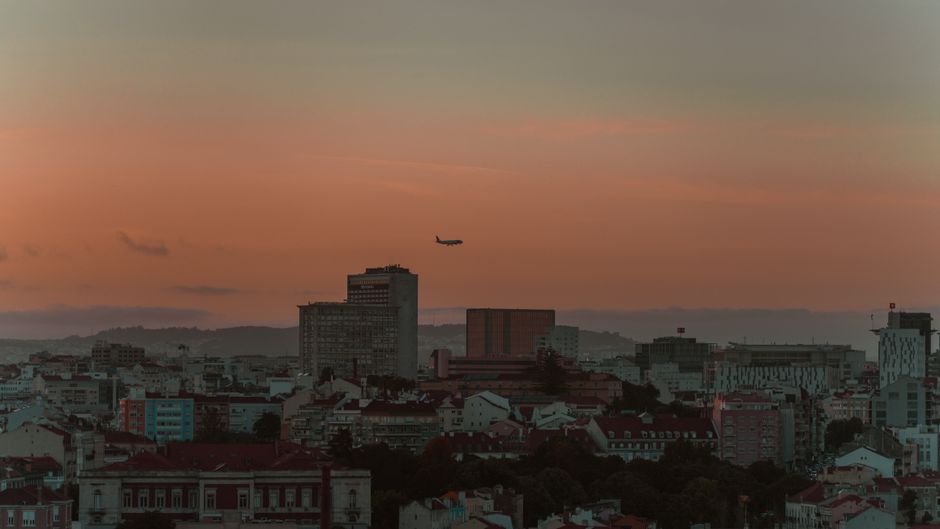 A serene view of Lisbon's skyline at sunset with an airplane in flight.