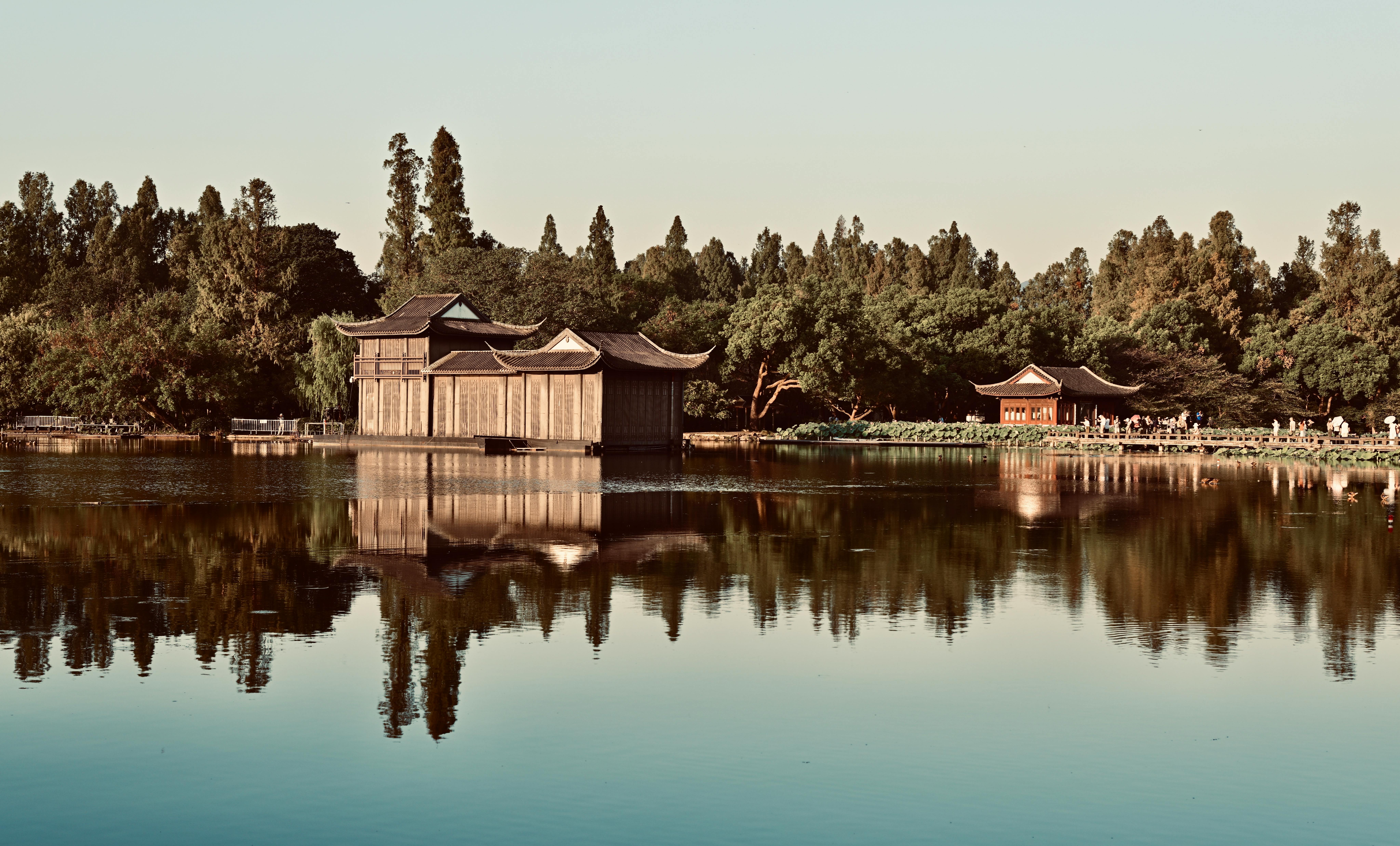 Peaceful reflection of traditional buildings on West Lake in Hangzhou, enveloped by lush greenery.