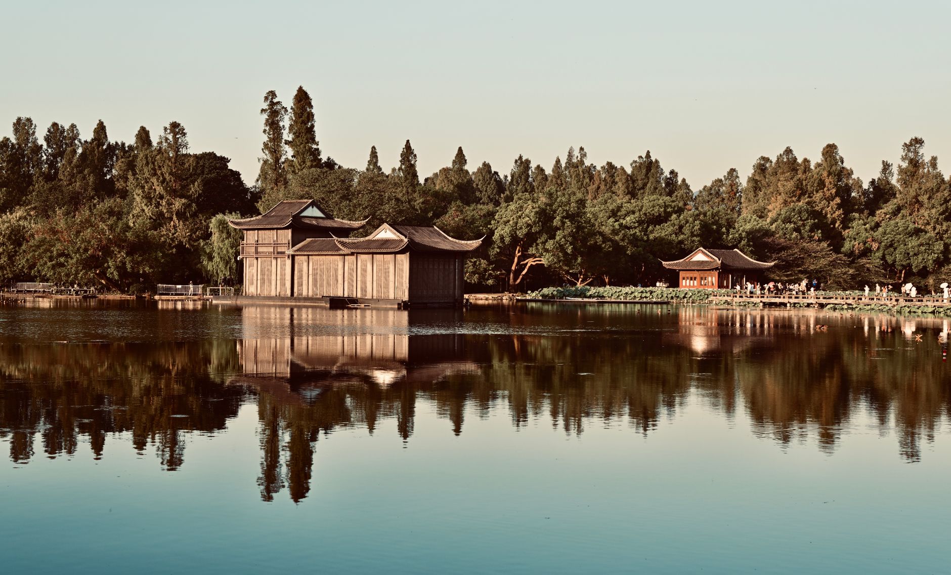 Peaceful reflection of traditional buildings on West Lake in Hangzhou, enveloped by lush greenery.