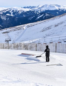 A person smoothing snow on a winter ski slope with mountains in the background.