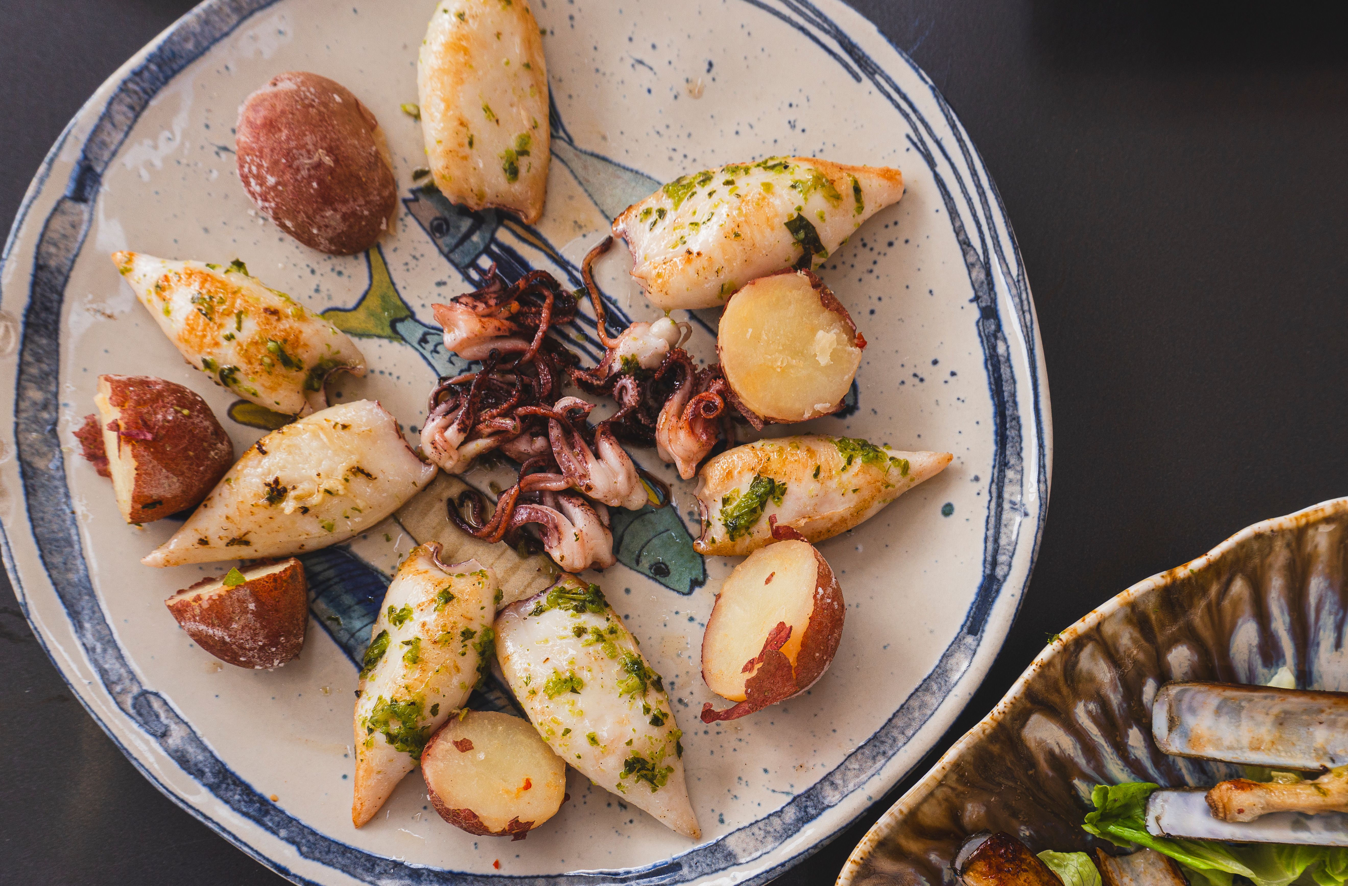 Top view of grilled calamari and potatoes on a ceramic plate, garnished with herbs.