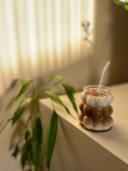 Free Aesthetic iced coffee served in a modern bubble glass on a minimalistic indoor setup. Stock Photo
