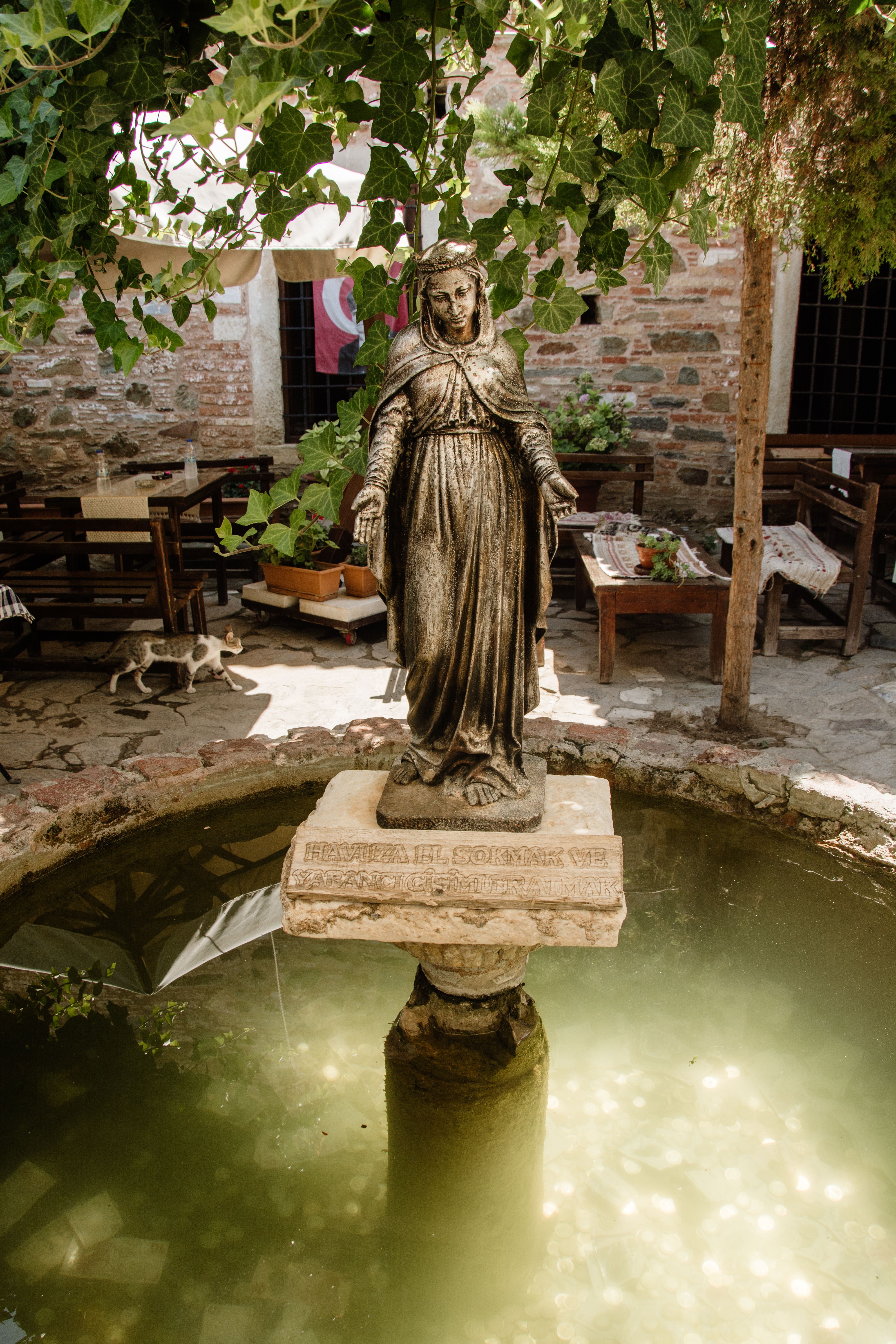 Elegant statue in a courtyard fountain with lush greenery and rustic decor.