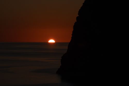 Free Captivating sunset over the ocean with a silhouetted cliff, creating a dramatic and tranquil scene. Stock Photo