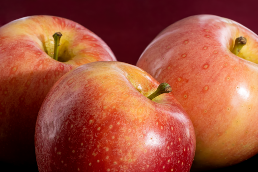 Vibrant, fresh red apples with a glossy sheen, showcasing natural texture and colors against a dark background.