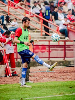 A football player practices juggling on the sidelines during a match.