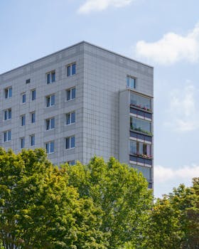 A modern residential building framed by vibrant trees under a clear blue sky.