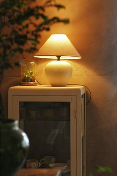 Warmly lit indoor scene featuring a table lamp on a cabinet with decor items.
