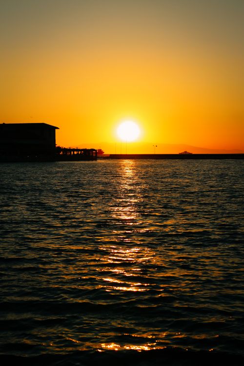 Free Stunning sunset over the ocean with vivid colors and silhouetted buildings on the horizon. Stock Photo