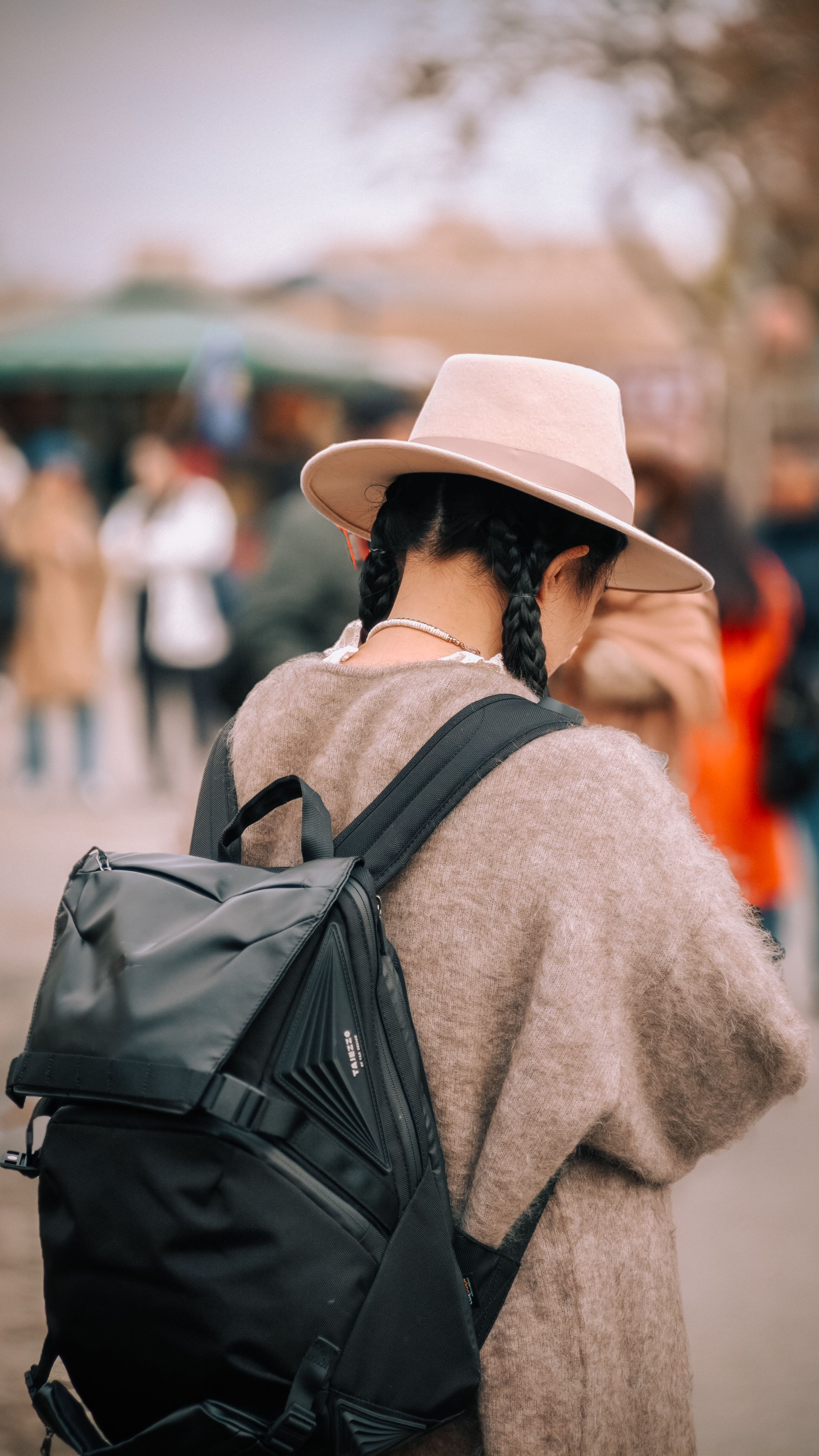 Mulher de chapéu e mochila explorando uma rua movimentada em Çin. Clima de aventura e exploração.
