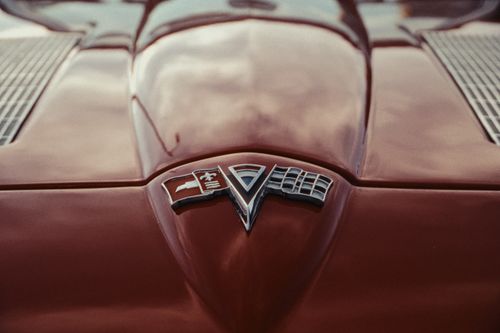 Free Close-up of a vintage red car hood featuring a classic emblem, reflective of 1960s design and aesthetics. Stock Photo