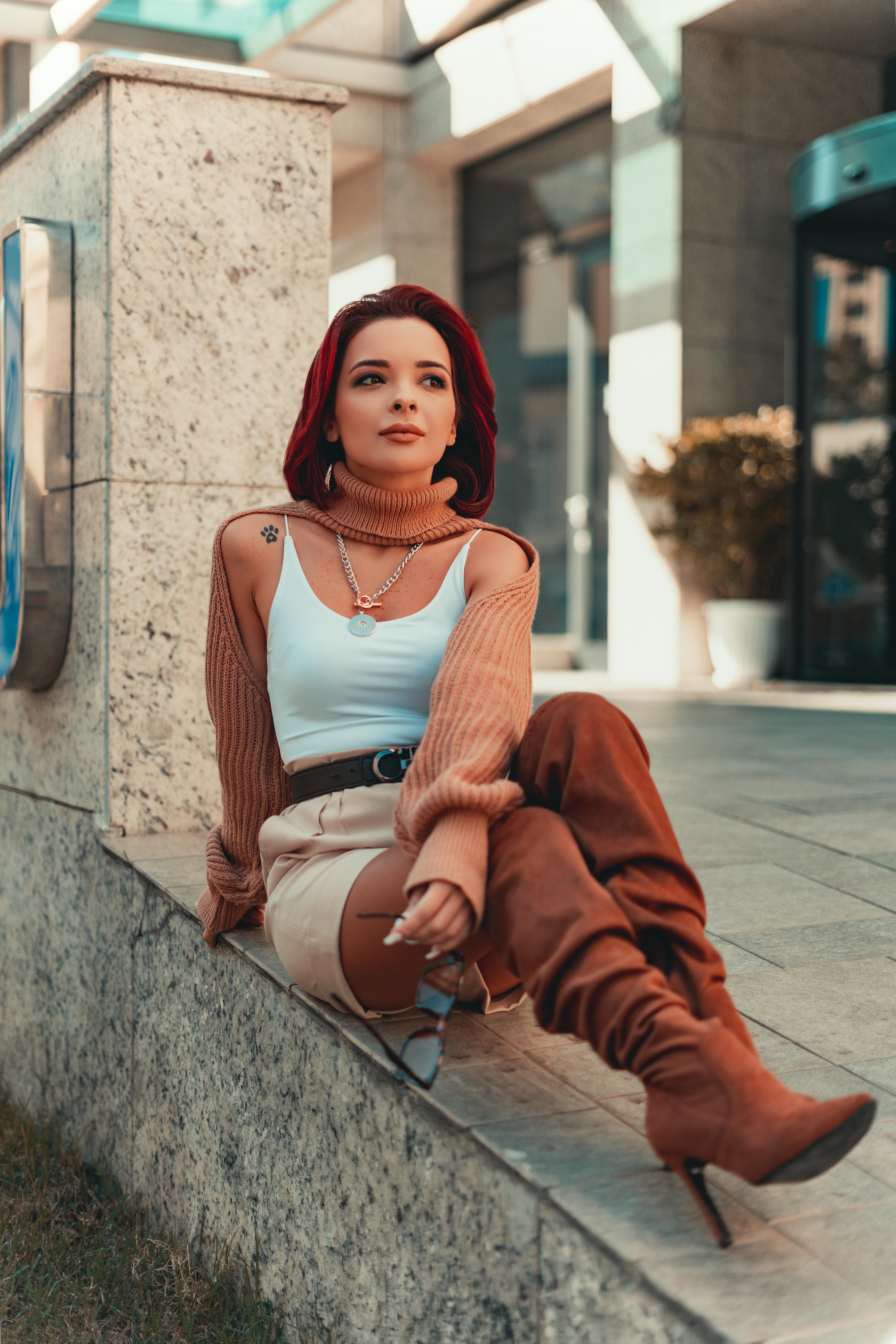 Woman with red hair in stylish outfit sitting outdoors on urban steps.