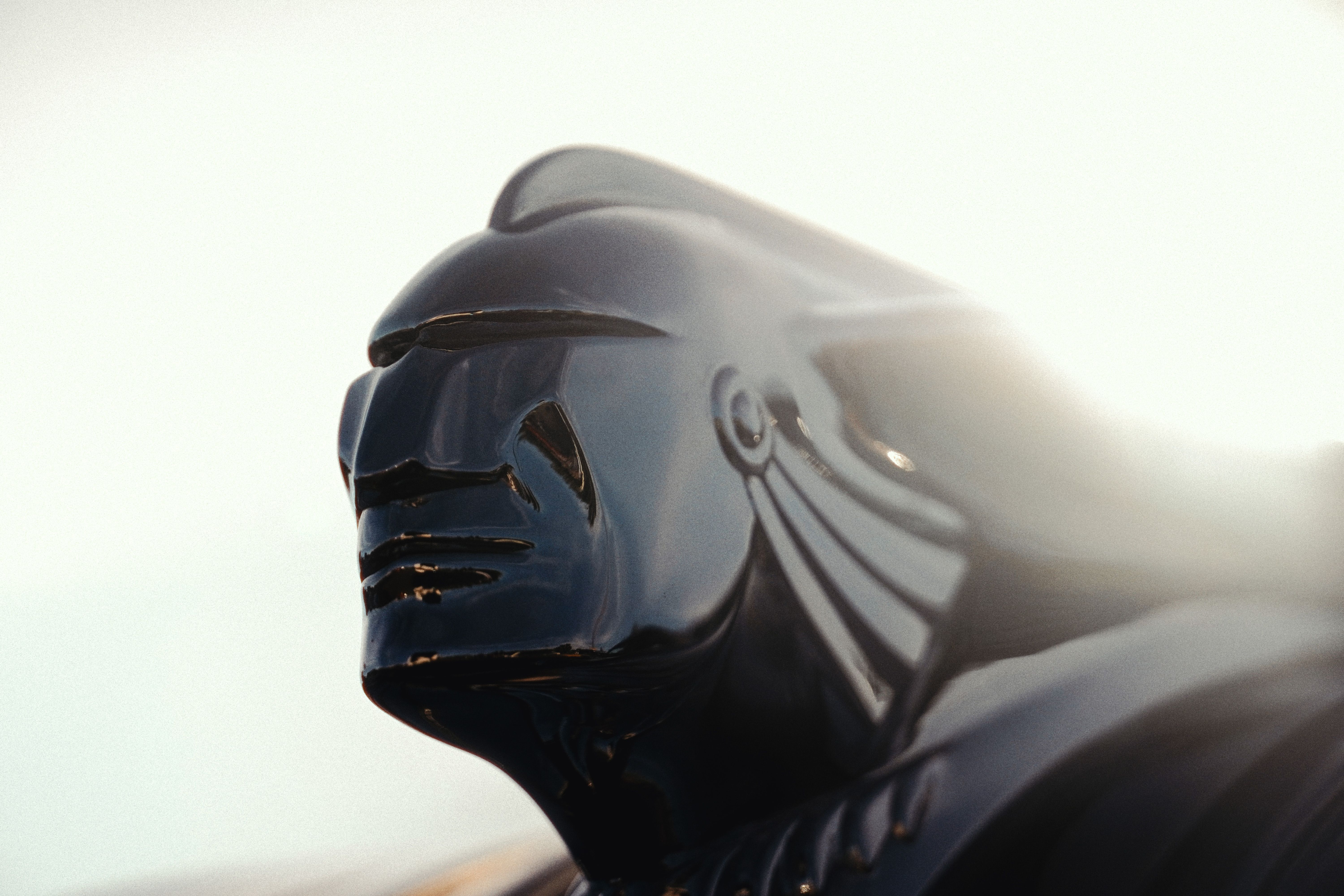 Dramatic close-up of a vintage car hood ornament, highlighting its intricate design under bright light.