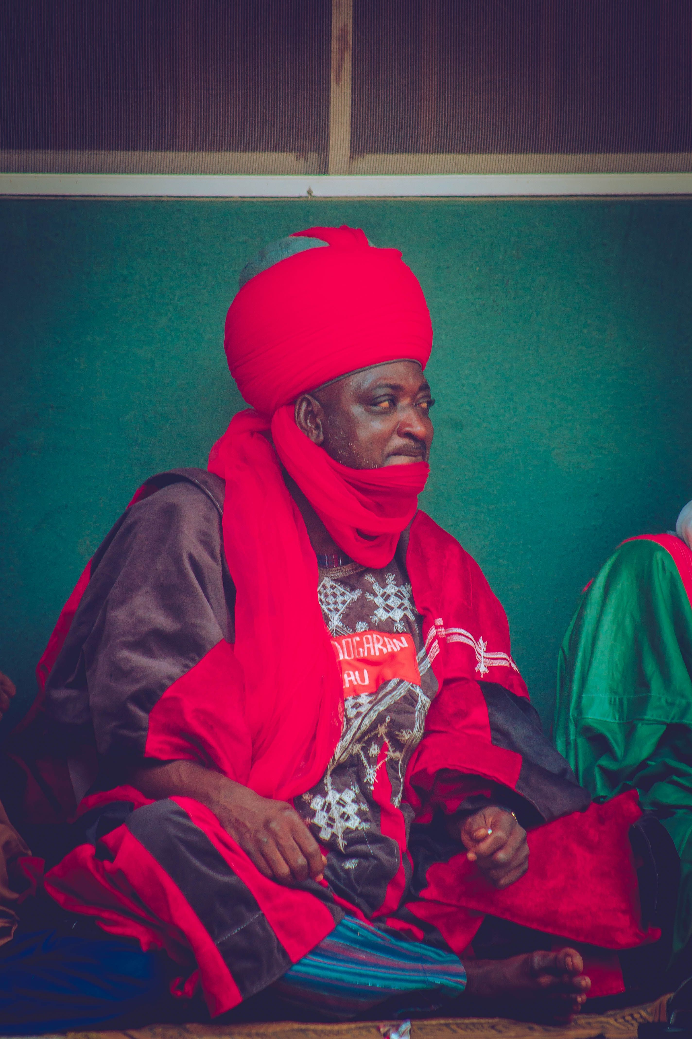 Man in traditional Nigerian attire with red turban and robe, conveying cultural richness.