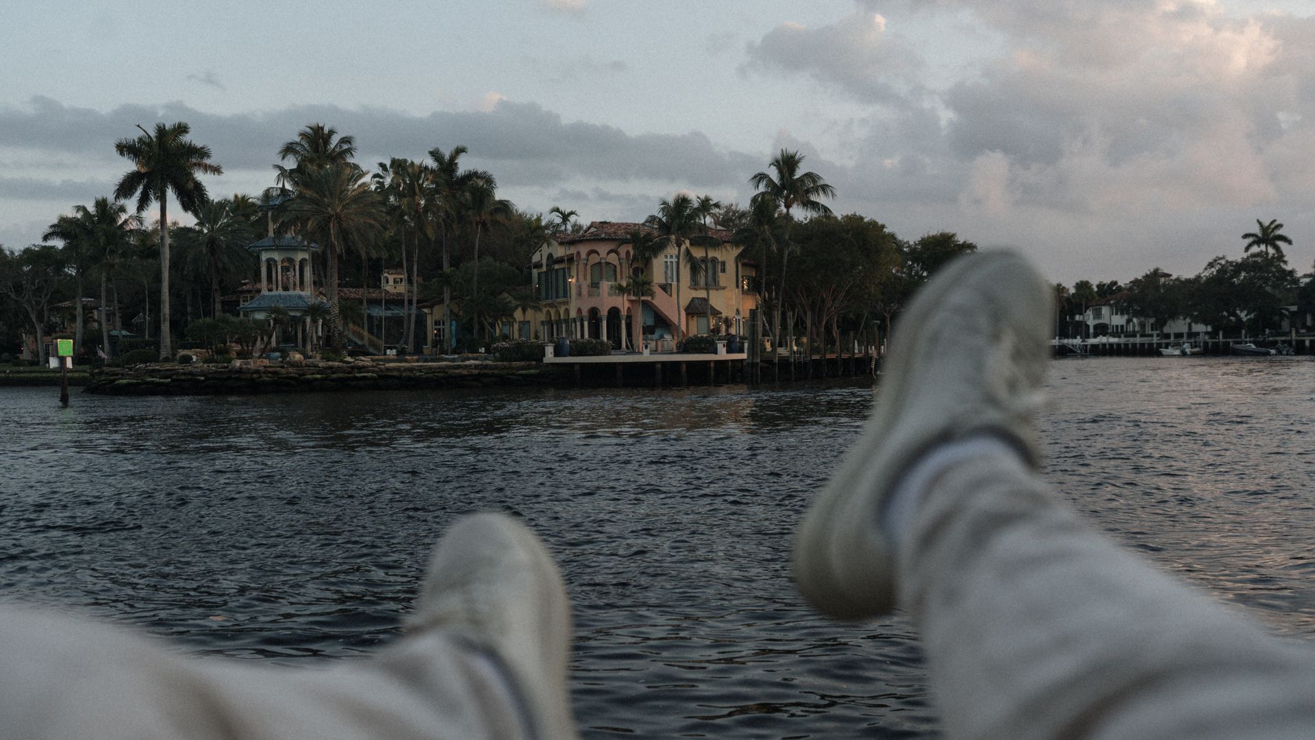 Casual perspective of a tropical waterfront villa with palm trees at sunset.
