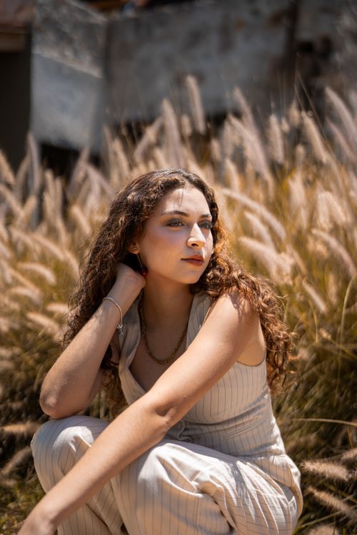 Free A woman sits in a field of grasses, enjoying a sunny day with a serene expression. Stock Photo