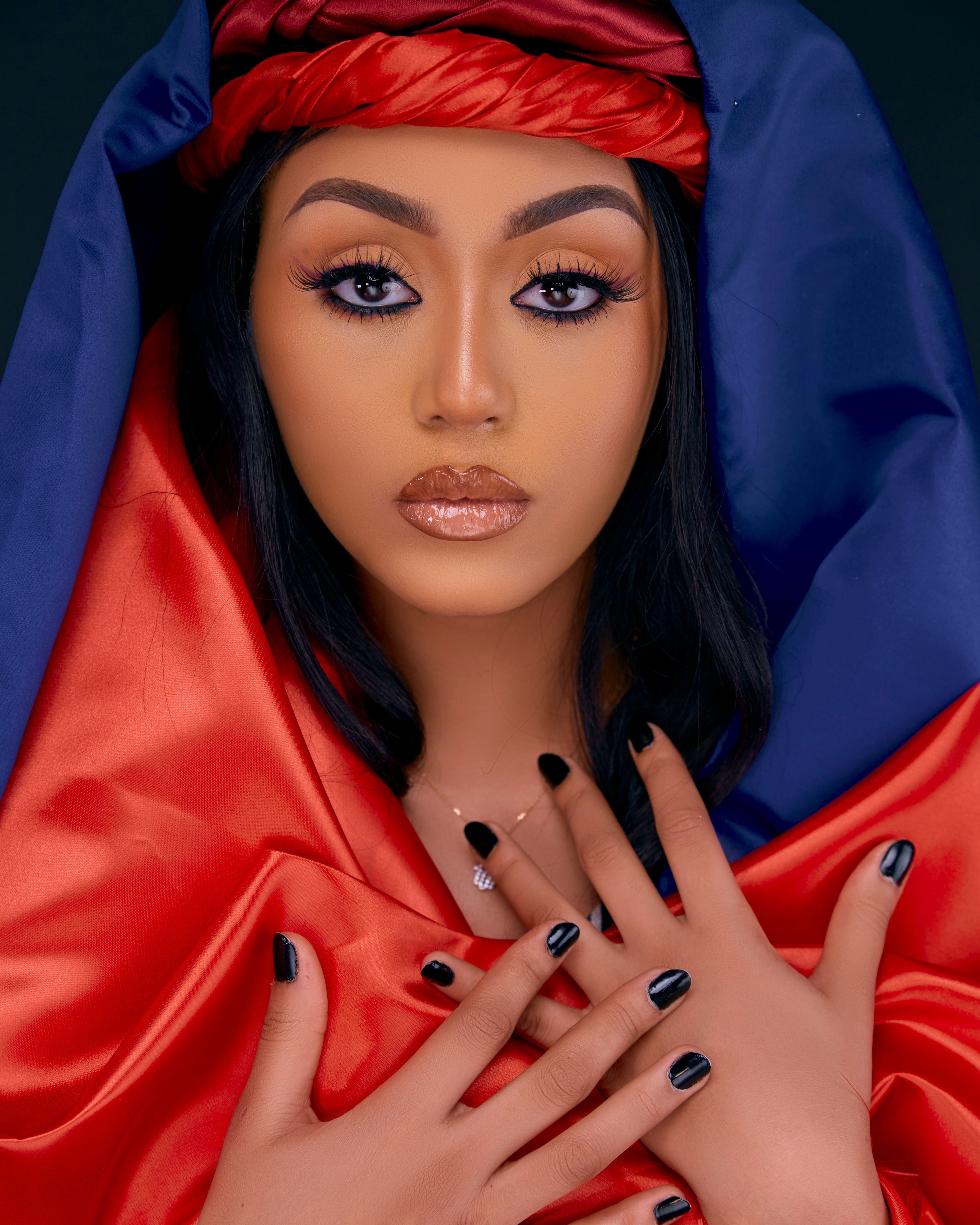 Striking portrait of a woman wrapped in red and blue fabric, featuring bold makeup and expressive eyes.