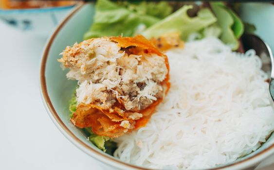 Delicious crispy spring roll served with rice vermicelli and fresh greens in a bowl.