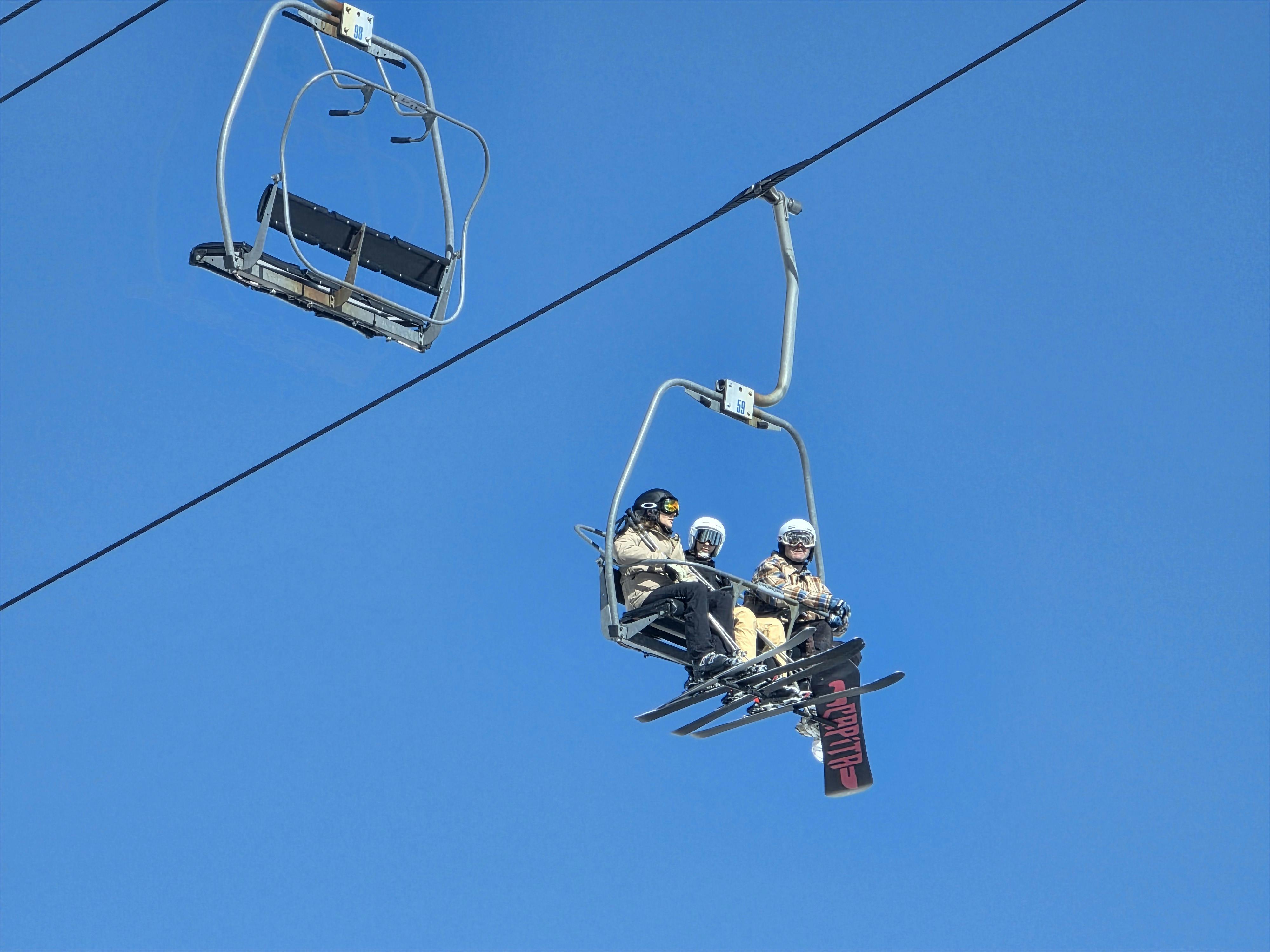 Three skiers on a chairlift enjoying a sunny winter day against a bright blue sky.
