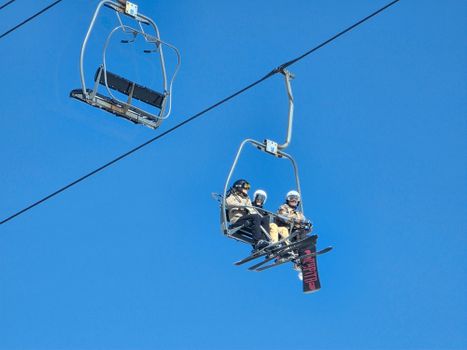 Three skiers on a chairlift enjoying a sunny winter day against a bright blue sky.
