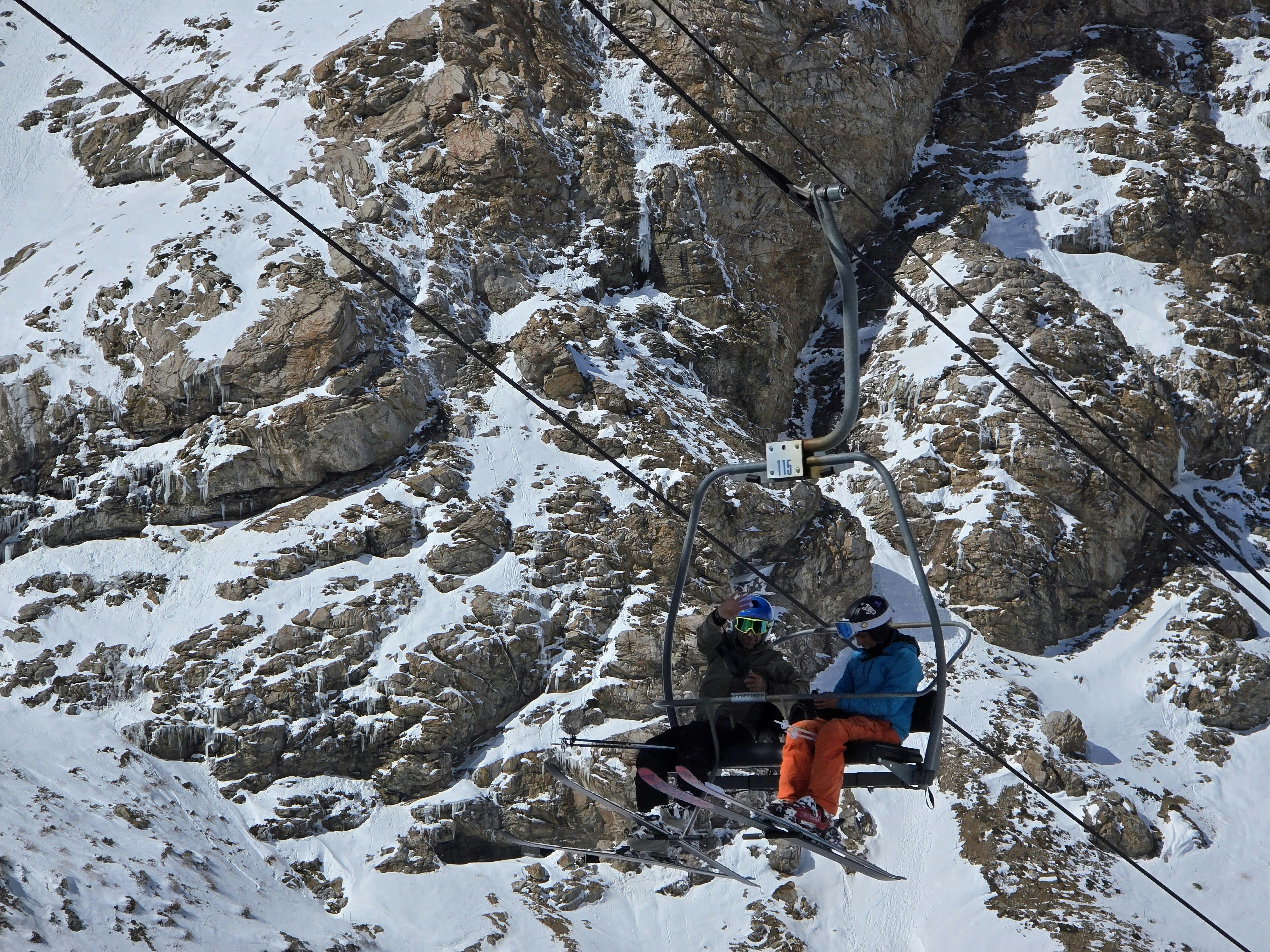 Two skiers in colorful attire ride a chairlift over a snow-covered mountain landscape.