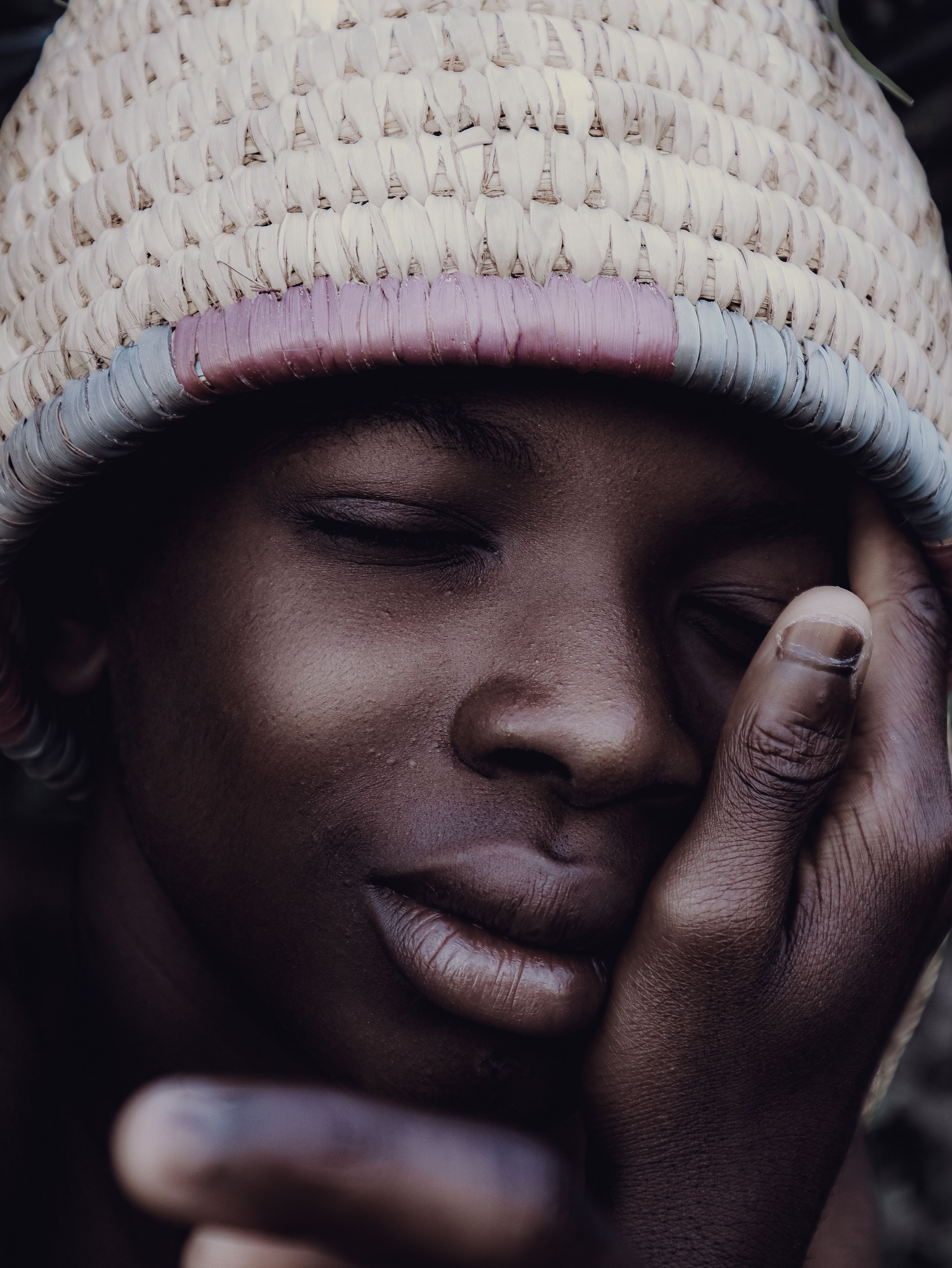 Close-up portrait of a young African boy wearing a woven hat with eyes closed.