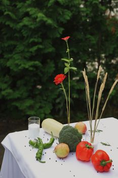 A vibrant outdoor still life with vegetables, flowers, and a white cloth on a table.