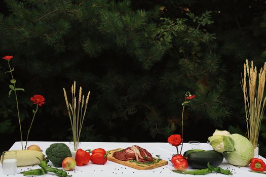 A rustic food table setup outdoors showcasing fresh vegetables and cuts of meat.