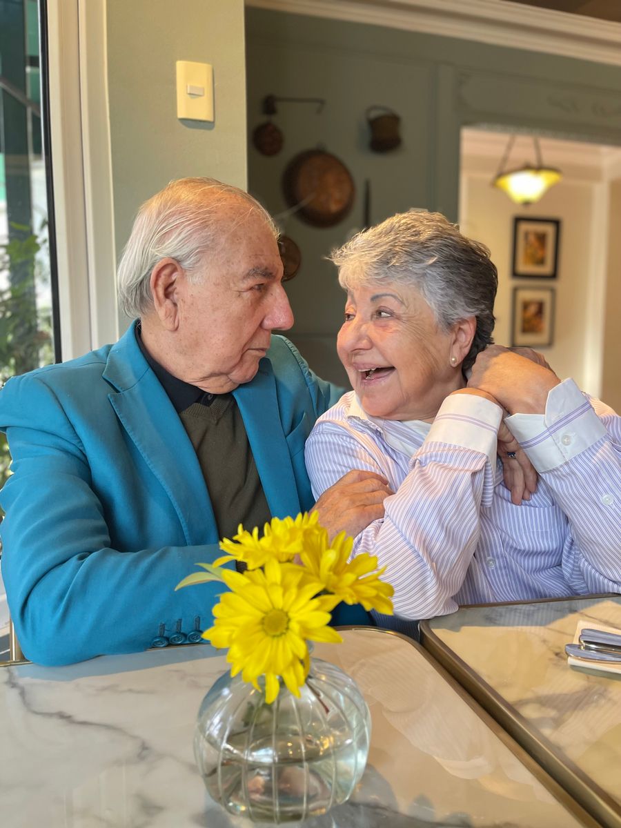 A senior couple laughing together with their caregiver at the table