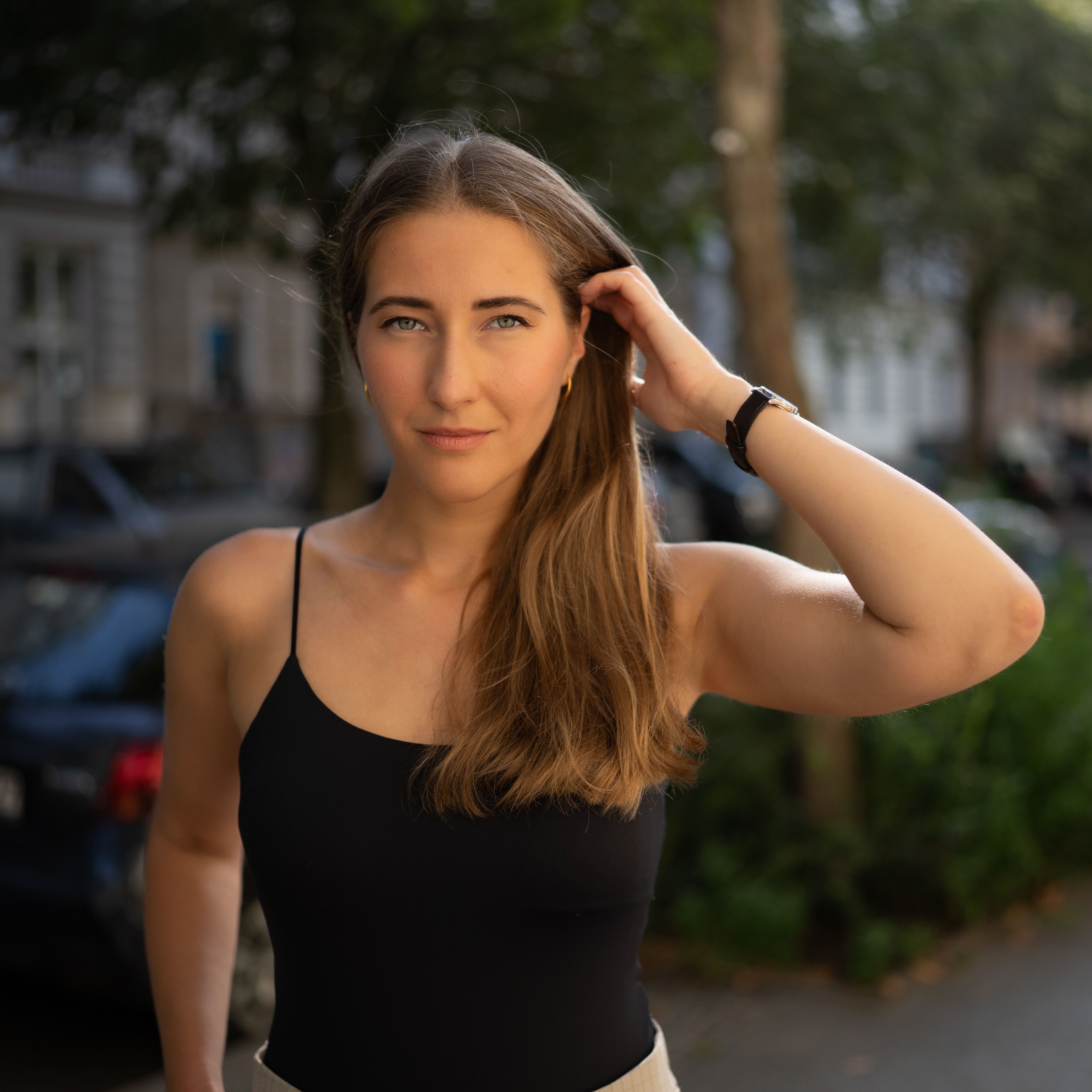 Woman with long hair wearing a black tank top poses confidently outdoors.